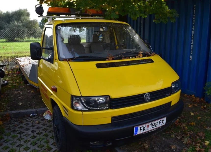 Der gelbe Abschleppwagen der Werkstatt mit Rundumleuchte vor dem blauen Lagercontainer